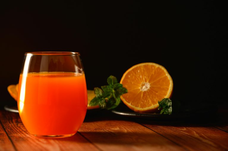 A close-up of fresh orange juice with a vibrant orange slice and mint leaves.