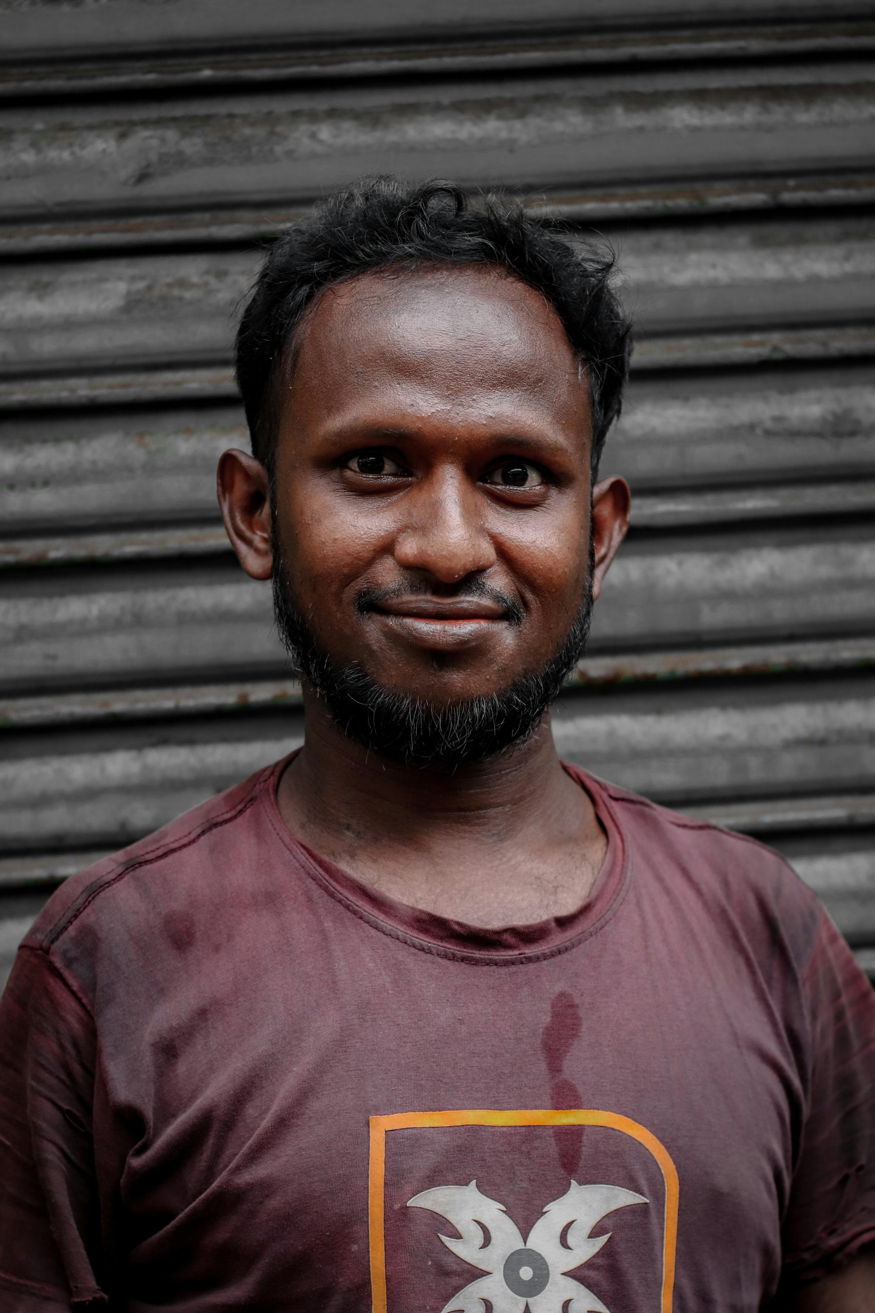 Portrait of an adult man smiling in front of a metal shutter.